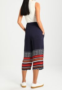 Marina culotter med randig nederkant som har röda, beige och vita vågmönster. Tillverkade av lättviktsmaterial och designade med fickor.