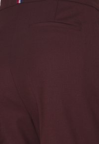Bordeaux broek van een textuurstof, met zijzakken en een achterzak, geaccentueerd met een multikleurige riemlus detail.