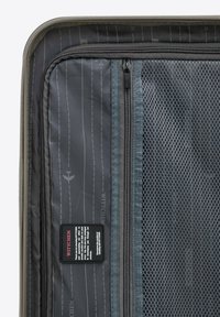 Interno di una valigia da viaggio grigia con tasca in rete, scomparti organizzati, motivo a righe verticali e un'etichetta con il marchio contenente istruzioni per la cura.