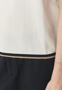 Top lavorato a maglia con una parte superiore bianca e una parte inferiore nera, caratterizzato da una sottile striscia orizzontale color beige al cucitura. Texture liscia, design casual.