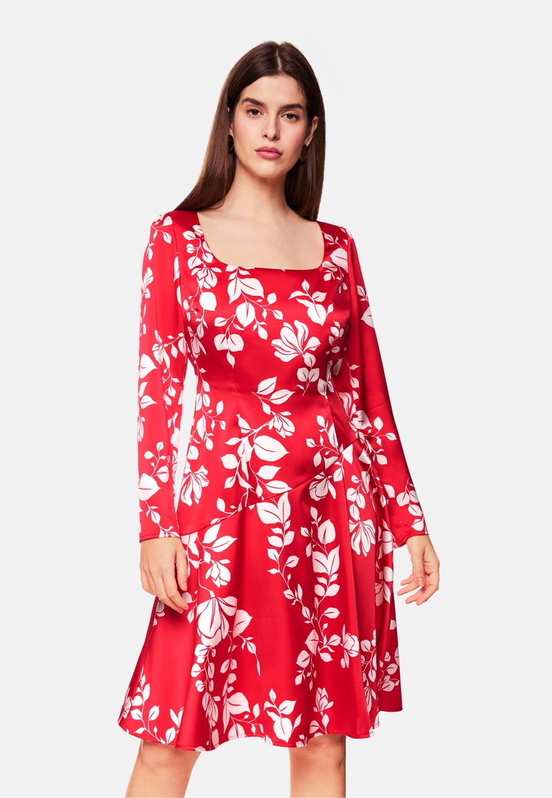 Rotes Blumenkleid mit quadratischem Ausschnitt, langen Ärmeln und einem schwingenden Rock. Es hat weiße Blättermuster auf dem Stoff.