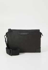 Black leather crossbody bag with a textured finish, featuring a zip closure and adjustable strap. Logo patch on the front. Rectangular shape.