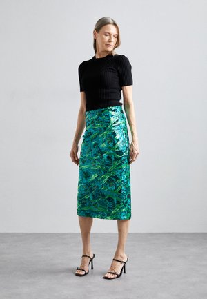 Top negro de manga corta con relieve, combinado con una falda midi estampada con lentejuelas en verde y turquesa. Sandalias de tacón alto negras y con tiras completan el conjunto.