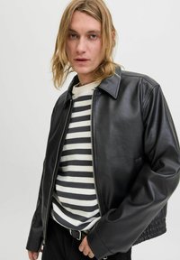 Chaqueta de cuero negra con un diseño de cuello, cierre de cremallera y un brillo sutil, llevada sobre un suéter de punto a rayas.