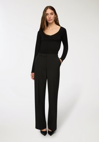 Czarny dopasowany sweter z dekoltem w serek i prążkowaną teksturą, w połączeniu z dopasowanymi czarnymi spodniami z kieszeniami i prostymi nogawkami.