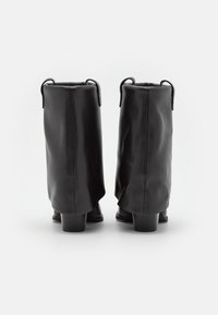 Czarne skórzane botki za kostkę o miękkim wykończeniu, z zaokrąglonym noskiem i krótkim, kwadratowym obcasem; wyposażone w uchwyty u góry ułatwiające zakładanie.