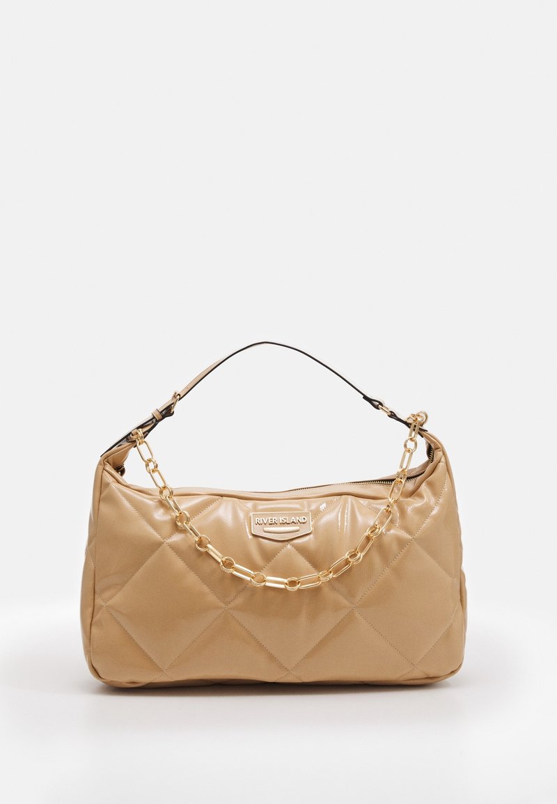 Quiltowany beżowy torebka z błyszczącym wykończeniem. Posiada złotą łańcuszkową rączkę oraz czarny akcent w postaci uchwytu. Logo wyraźnie wyeksponowane.
