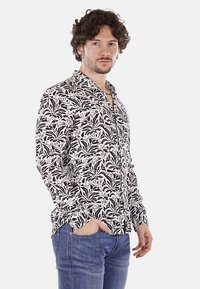 Camicia a maniche lunghe a motivo floreale in bianco e nero, con colletto a bottoni, taglio slim e tessuto morbido. Abbinata a jeans blu.
