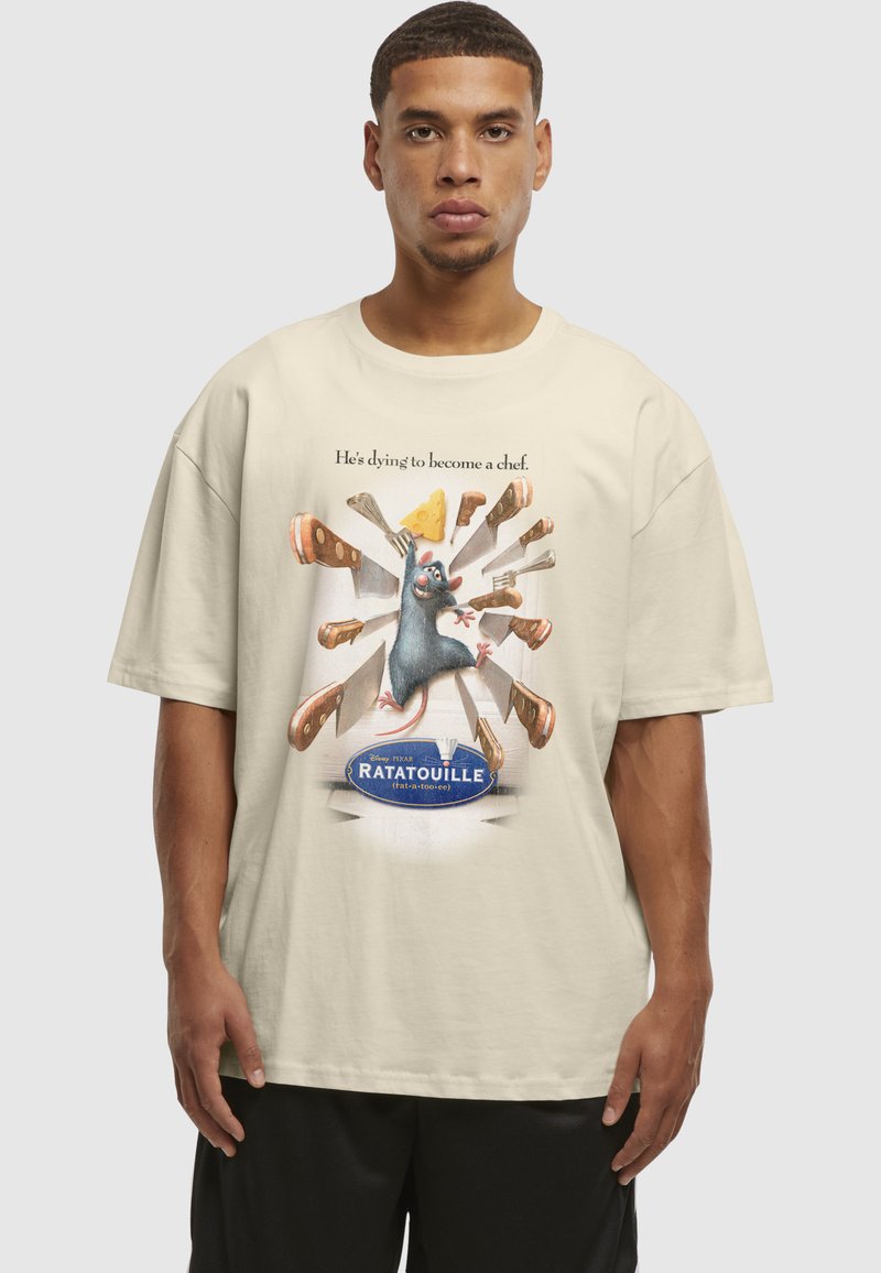 Homme portant un t-shirt beige avec le personnage de rat de « Ratatouille » entouré de couteaux et de fromage, avec la légende « Il meurt d'envie de devenir chef. »