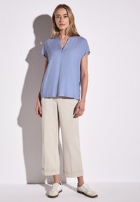 Blusa azzurro chiaro a maniche corte con scollo a V, abbinata a pantaloni beige larghi e sneakers bianchi. Tessuto morbido e vestibilità comoda.