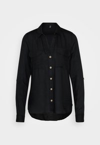 Chemise noire à boutons, fabriquée dans un tissu doux et texturé. Présente un décolleté en V, deux poches poitrine et des boutons en ton doré. Manches longues avec poignets.