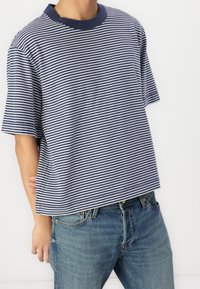Camiseta de manga corta a rayas en navy y blanco con un escote redondo, que presenta un corte relajado y una textura de algodón suave. Combinada con unos jeans de color azul claro.