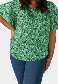Zelený květinový top s krátkým rukávem a volným střihem, zdobený směsí malých modrých a bílých vzorů na živém zeleném pozadí.