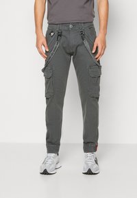 Pantalones cargo de tela gris oscuro con múltiples bolsillos laterales, correas ajustables y un diseño de pierna ajustada. Combinados con zapatillas grises.