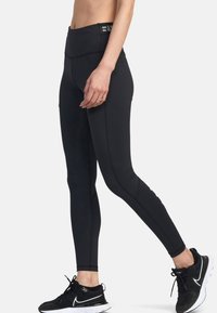 Leggings neri a vita alta con una texture liscia, caratterizzati da cuciture a contrasto e una vita elastica, completati da scarpe da ginnastica nere.