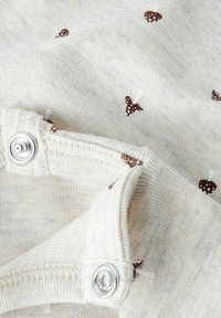 Jasnobeżowa tkanina z małymi brązowymi wzorami grzybów, z zapięciem na napy i miękkim, teksturowanym bawełnianym materiałem.