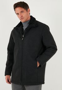 Černý prošívaný kabát s vysokým límcem, zapínáním na zip a bočními kapsami. Vyrobený z texturované látky, s klasickým obdélníkovým střihem.