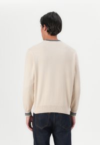 Béžový pletený sveter s rebrovanými manžetami, ktorý má zelené a námornícke pruhy. Jednoduchý, klasický dizajn s okrúhlym výstrihom a štandardným strihom.