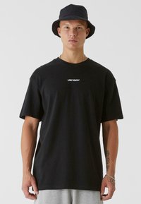 Black cotton t-shirt with short sleeves, featuring a white text logo "LOST YOUTH" across the chest. Worn with a black bucket hat.
