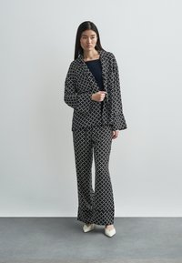Black and white patterned blazer and trousers set, featuring a geometric design. The fabric appears smooth, and the cut is relaxed.