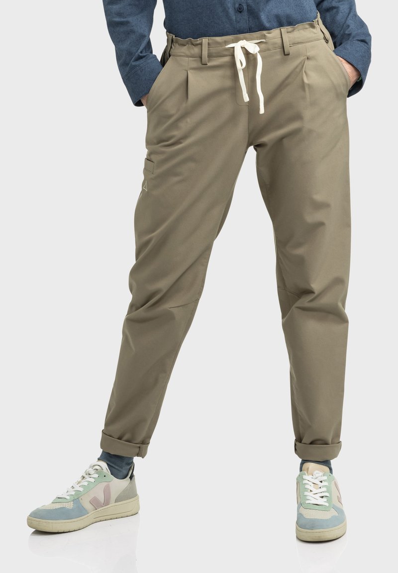 Beige, taillierte Hose mit einem Kordelzugbund, Falten und Seitentaschen. Getragen mit mehrfarbigen Turnschuhen und einem blauen Hemd.