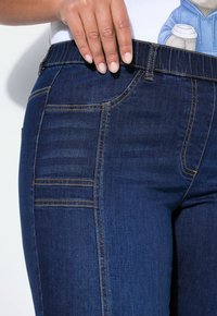 Tmavě modré džíny z denimu s elastickým pasem, ozdobené jemným prošíváním kapes a hladkým, strukturovaným povrchem.