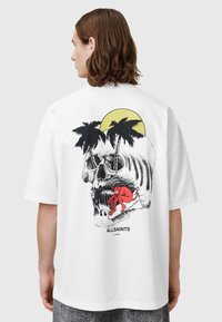 Hvit t-skjorte med et grafisk design av et skjelett, palmer og en rød figur som surfer, med teksten "ALLSAINTS" nederst.