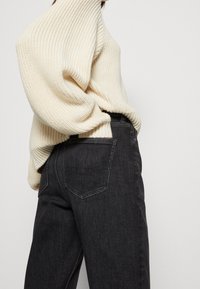 Pull en maille crème avec texture côtelée associé à un jean noir taille haute, doté de poches arrière et d'une coupe droite.