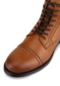 Hnedé kožené topánky s okrúhlou špičkou, textúrovaným povrchom, tmavohnedými šnúrkami a detailmi prešitia, s nízkou čiernou gumovou podrážkou.