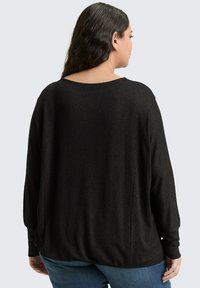 Zwarte lange mouwen top met een ronde halslijn, losse pasvorm en een zachte textuur. Heeft verlaagde schouders en een gebogen zoom.