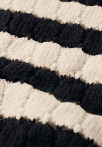 Schwarz-weißen gestreiften Teppich mit einer strukturierten, plüschigen Oberfläche. Abwechselnde breite Streifen mit erhabenen Punkten und einem weichen, wollähnlichen Material.