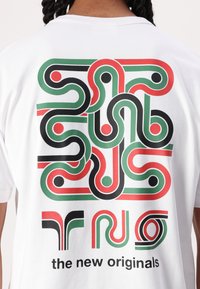 Hvit bomulls t-skjorte med et fargerikt abstrakt grafisk design i rødt, grønt og svart på baksiden med tekst: "de nye originalene."