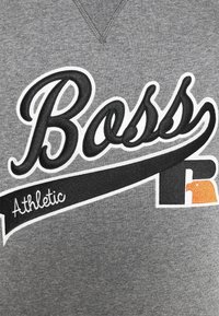 Tissu gris avec texte brodé en noir et blanc "Boss Athletic" et logo stylisé "R" en noir et orange.