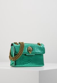 La borsa a mano verde metallica presenta un motivo a serpente testurizzato, una tracolla in catena dorata e una chiusura a conchiglia decorativa. Ha una forma rettangolare con cappuccio superiore.