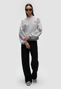 Felpa grigia con spalle ribassate e logo ricamato, abbinata a pantaloni larghi neri e scarpe con plateau argentate.