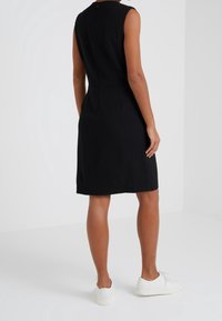 Musta ilmanhiha dressi, jossa on hyvä istuvuus, polvipituus, huomaamattomat laskokset vyötäröllä ja takavetoketju. Yhdistetty valkoisiin lenkkareihin.