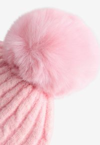 Bonnet en laine rose tricoté avec une texture côtelée épaisse et un grand pompon rose duveteux sur le dessus. Matériau doux et chaud.
