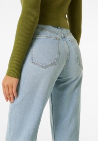 Ljusblå denimjeans med en avslappnad passform, som har två bakfickor och subtila sömnadsdetaljer, kombinerade med en räfflad olivgrön topp.