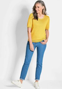 Gelbes, kurzärmliges Strickoberteil mit Rundhalsausschnitt, kombiniert mit hellblauen Slim-Fit-Jeans und weißen Sneakers. Lässiges und bequemes Outfit.