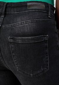 Svarta denimjeans med en något urtvättad textur, med en enda bakficka och en läderetikett på midjebandet.