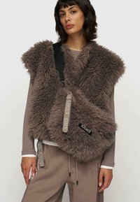 Faux fur vest i afdæmpet brun med et lagdelt design, der har en sort justerbar rem og logo-accenter. Sammen med matchende bukser.
