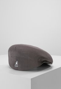 Kangol baretka v šedé barvě, vyrobená z prodyšného pleteného materiálu, má zaoblený tvar s plochou korunou a malou logovou akcentací.