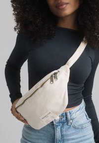 Canvas crossbody bag in off-white with gold zipper, triangular shape, and textured fabric; features a small label with "HOLZRICHTER."