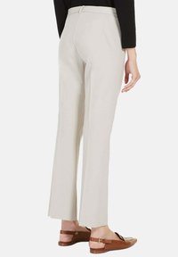 Beige op maat gemaakte trousers met een uitlopende zoom, ceintuurlussen en een gladde textuur, gecombineerd met bruine instapsandalen.