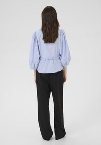 Bluza cu dungi, albastru deschis, cu mâneci bufante, talie strânsă și croială lejeră, asortată cu pantaloni negri cu picioarele largi. Textură netedă a țesăturii.