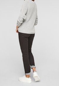 Hellgrauer Strickpullover, dunkelbraune Hosen mit umgeschlagenem Saum und weiße Turnschuhe mit silbernem Akzent an der Ferse. Lässiges Outfit von hinten gesehen.