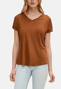 Braunes kurzärmliges V-Ausschnitt-T-Shirt aus glattem Stoff, mit umgeschlagenen Ärmeln und lockerer Passform, kombiniert mit hellblauen Jeans.