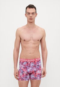 Férfi boksznadrág rózsaszín derékrésszel, amelyen a "BJÖRN BORG" felirat szerepel. Sűrűn mintázott pálmafákkal élénk rózsaszín és lila árnyalatokban, sima anyagból készült.
