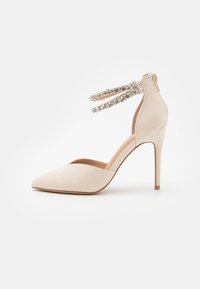 Scarpa con tacco alto in suede nuda, punta affusolata, cinghie alla caviglia adornate con strass trasparenti e tacco a stiletto sottile.