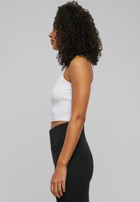 Witte cropped tanktop gecombineerd met hoge zwarte legging, met een gladde texture en een aangesloten design, van opzij getoond.